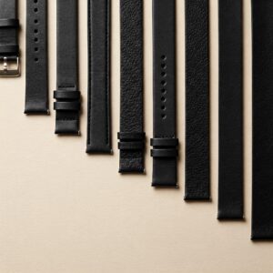 Various widths of black leather watch straps laid out side-by-side.